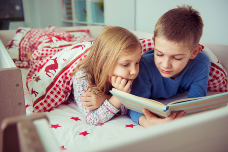 Two happy sibling children reading book in bunk bed under blanketの写真素材