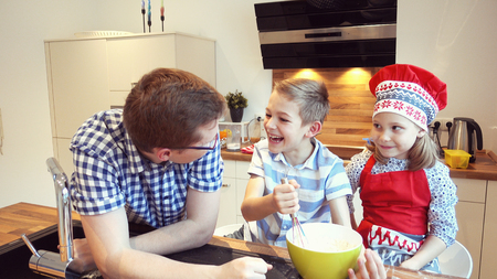 Young father with two happy children backing cookies and having fun in modern kitchenの写真素材