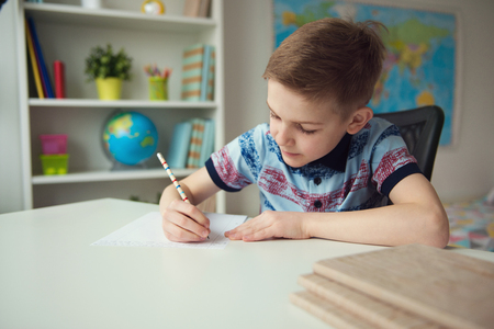 Little smart school boy making  homework at desk in his roomの写真素材