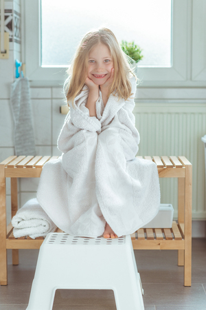 Portrait of pretty little child girl with white towel after shower  in bright bathroom at homeの写真素材