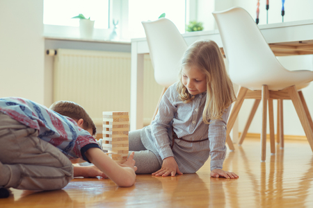 Two happy siblings playing a game with wooden blocks at home joyfully の写真素材
