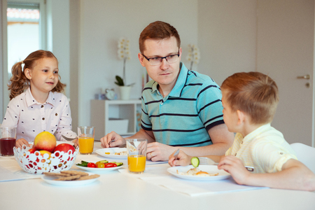 Happy father with his cute children talking at the breakfast at homeの写真素材