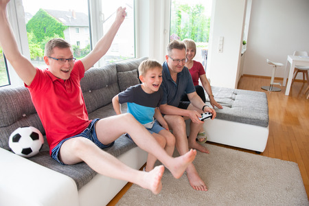 Grandparents, their son and grandson are playing computer game  emotionally at home on sofa
