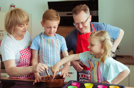 Happy grandparents have fun with their grandchildren preparing chocolate muffins at home in modern kitchenの写真素材