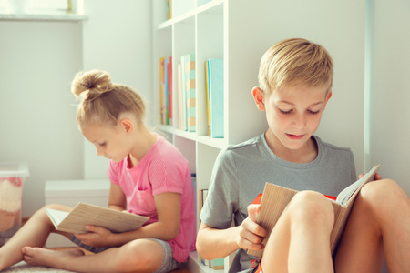 Two happy children reading books on the floor at the school  library