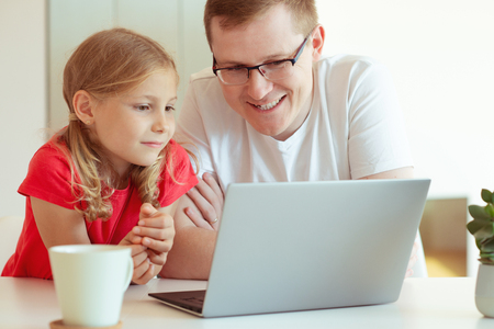 Happy young father have fun with his pretty little daughter during working with laptop at modern homeの写真素材