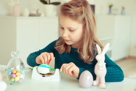 Cute little blonde girl painting Easter eggs at homeの写真素材