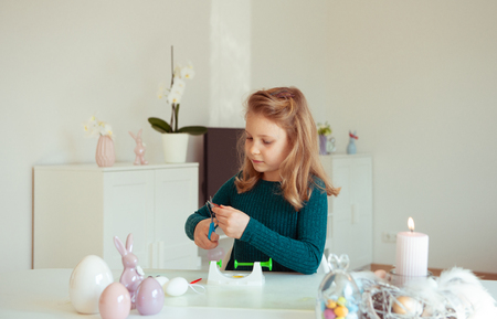 Cute little blonde girl painting Easter eggs at homeの写真素材
