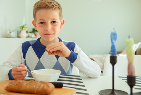 Handsome teenager eating soup and whole grain bread in bright living room at homeの写真素材