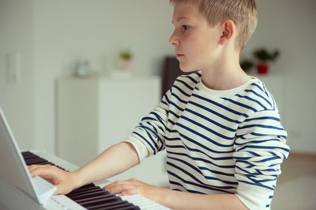 Teenager boy has training course with white e-piano at homeの写真素材