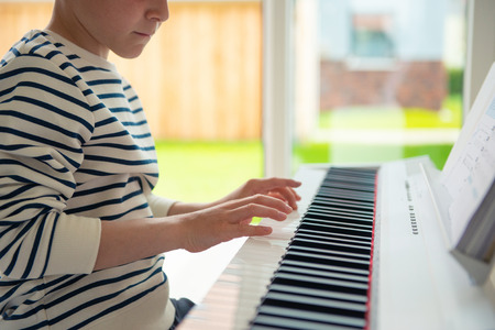 Teenager boy has training course with white e-piano at home