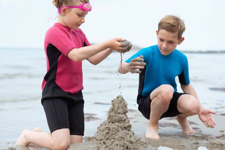 Two happy siblings children in neoprene swimsuits playing with sand in a Baltic seaの写真素材