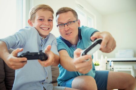 Happy young father and  his son playing computer games  with controllers very emotional in the...