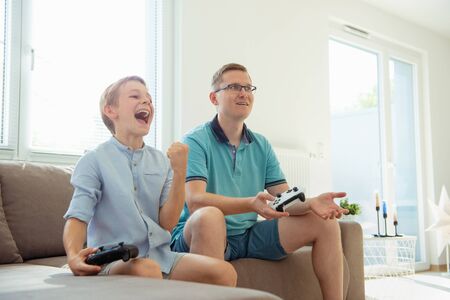 Happy young father and  his son playing computer games  with controllers very emotional in the...