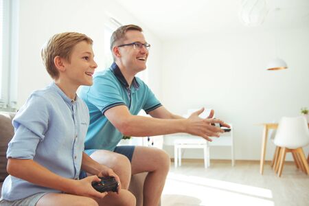 Happy young father and  his son playing computer games  with controllers very emotional in the...