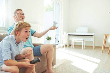 Happy young father and  his son playing computer games  with controllers very emotional in the...