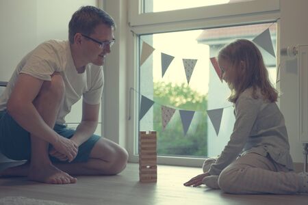Young happy father playing with his cute daughter with wooden blocks at homeの写真素材