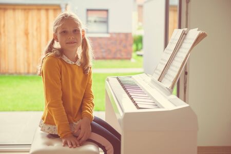 Portrait of pretty little girl having piano lesson at modern white e-piano at homeの写真素材
