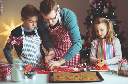 Happy young father with his cute children bakes ginger cookies for Christmas eve with christmas tree on backgroundの写真素材