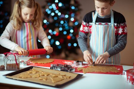 Happy teen siblings children preparing Christmas cookies at home with christmas tree on backgroundの写真素材