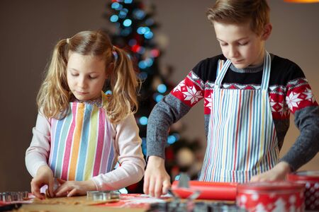 Happy teen siblings children preparing Christmas cookies at home with christmas tree on backgroundの写真素材