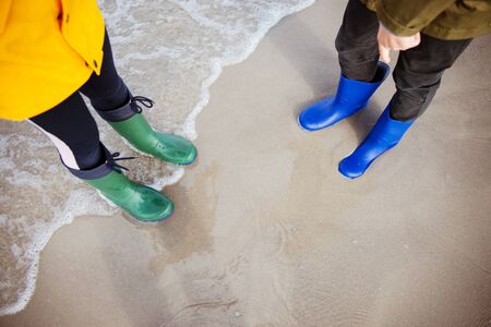 Two children standing im water of cold Baltic sea in colorful rubber high bootsの写真素材