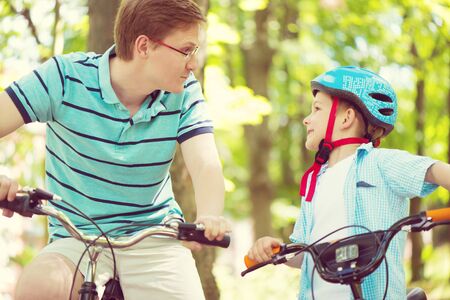 Happy father and son ride on bikes in summer parkの写真素材