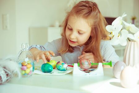 Cute little blonde girl painting Easter eggs at home