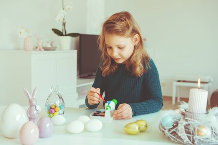 Cute little blonde girl painting Easter eggs at homeの写真素材