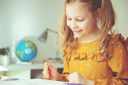 Pretty little girl paiting with colorful  crayon and paintbrush at the table at homeの写真素材