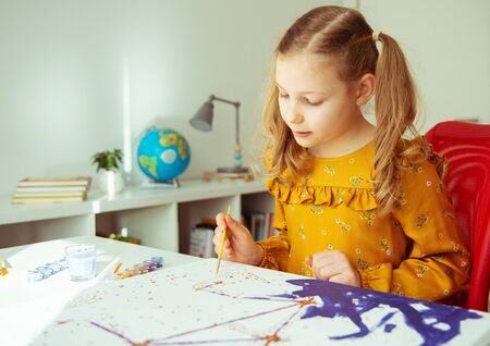 Pretty little girl paiting with colorful  crayon and paintbrush at the table at home