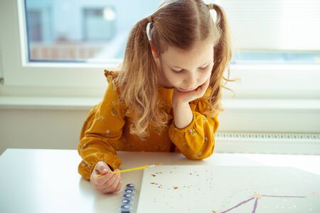 Pretty little girl paiting with colorful  crayon and paintbrush at the table at home