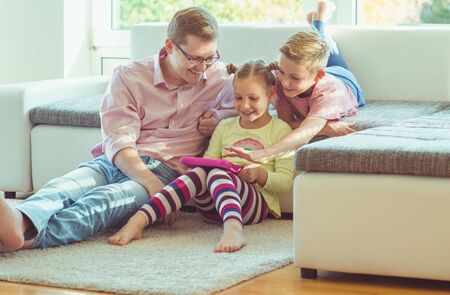 Happy young handsome father having fun with his two cute children playing joyful with tabletの写真素材