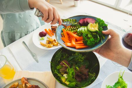 Fathers hand giving doughter salad at festive served table with healthy colorful vegetables and baked potato and chicken at family dinnerの写真素材