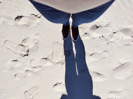 Photo of standing legs in jeans and sneakers on white sand. View from above