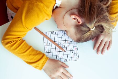 TIred teen girl solving sudoku at desk at school or at home. View from aboveの写真素材