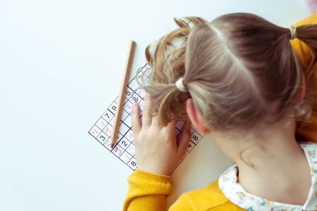 TIred teen girl solving sudoku at desk at school or at home. View from aboveの写真素材