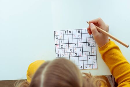 Adorable teen girl solving sudoku at desk at school or at home. View from aboveの写真素材