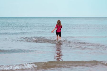 Happy little girl running in Baltic sea and playing with wavesの写真素材