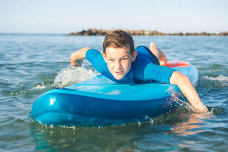 Happy teen child boy having fun and making sport on sup board in water in Baltic sea