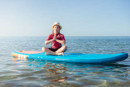 Cute teen child girl having fun and making yoga on sup board in water in Baltic seaの写真素材
