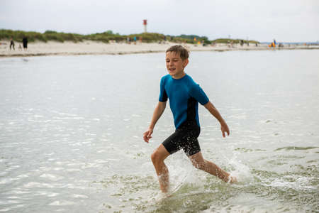 Portrait of emotional teen boy running in neoprene swimsuit in Baltic seaの写真素材