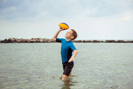 Happy handsome teen boy running and playing with ball in neoprene swimsuit in Baltic seaの写真素材