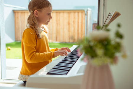 Portrait of pretty little girl having piano lesson at modern white e-piano at homeの写真素材