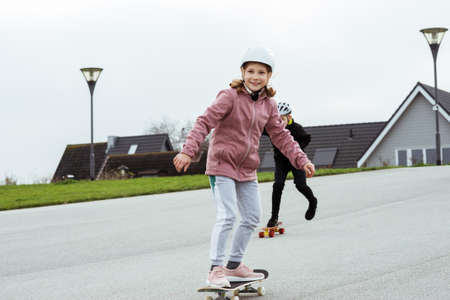 Happy teenagers boy and girl having fun skateboarding in street in helmetsの写真素材