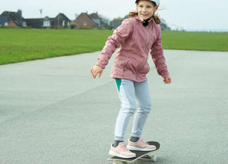 Adorable teenage girl drives with skateboard on smooth asphalt in white helmetの写真素材
