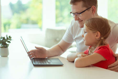 Happy young father with cute doughter learning together online at homeschoolingの写真素材