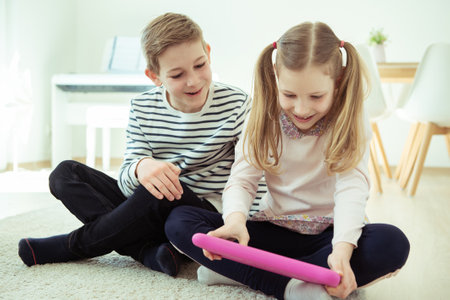 Portrait of happy siblings children playing with tablet on floor at modren homeの写真素材