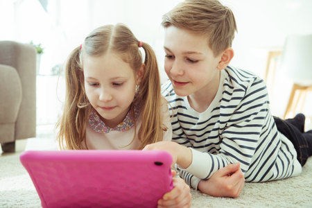Portrait of happy siblings children playing with tablet on floor at modren homeの写真素材