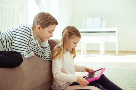 Portrait of happy siblings children playing with tablet on floor at modren homeの写真素材